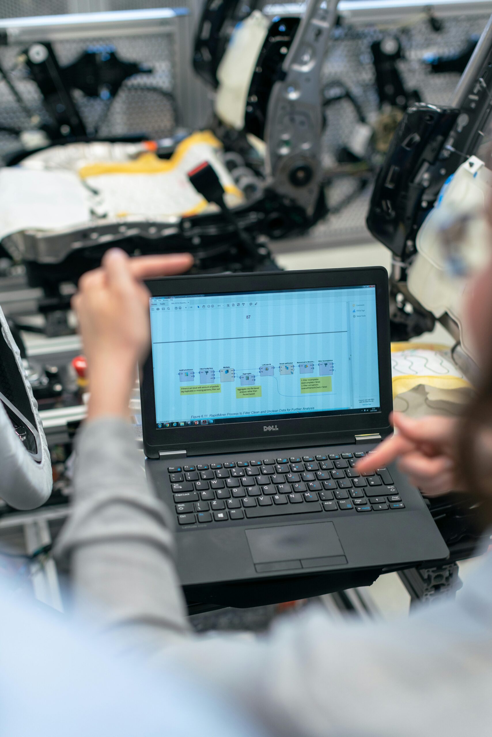 Engineers using a laptop to analyze software data in an industrial workshop setting.