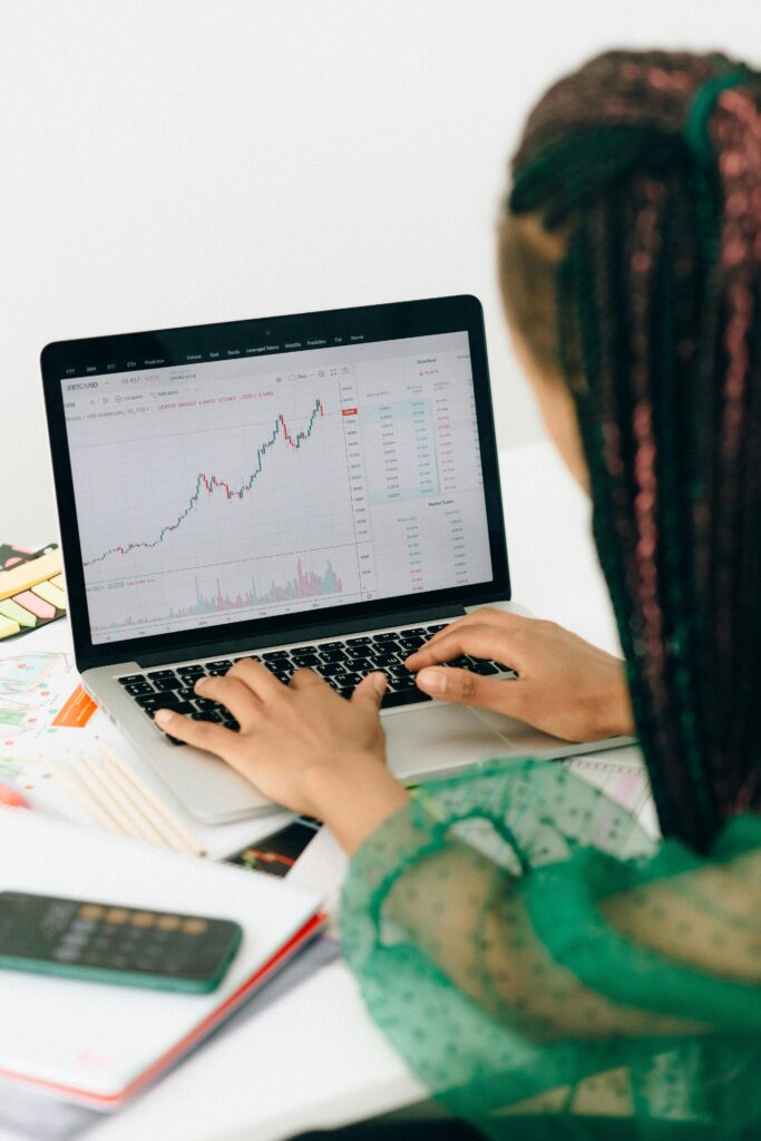 A woman working on financial analysis using a laptop with a stock market graph on screen.