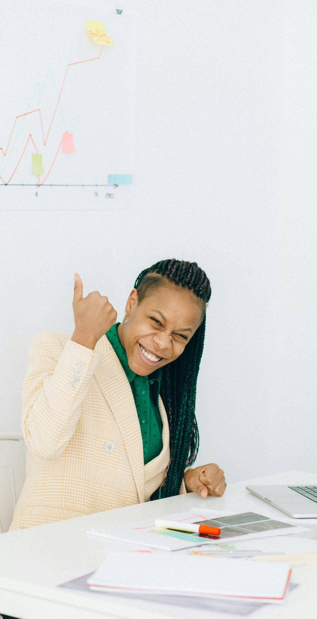 Smiling businesswoman gives thumbs up in an office setting, indicating success and achievement.